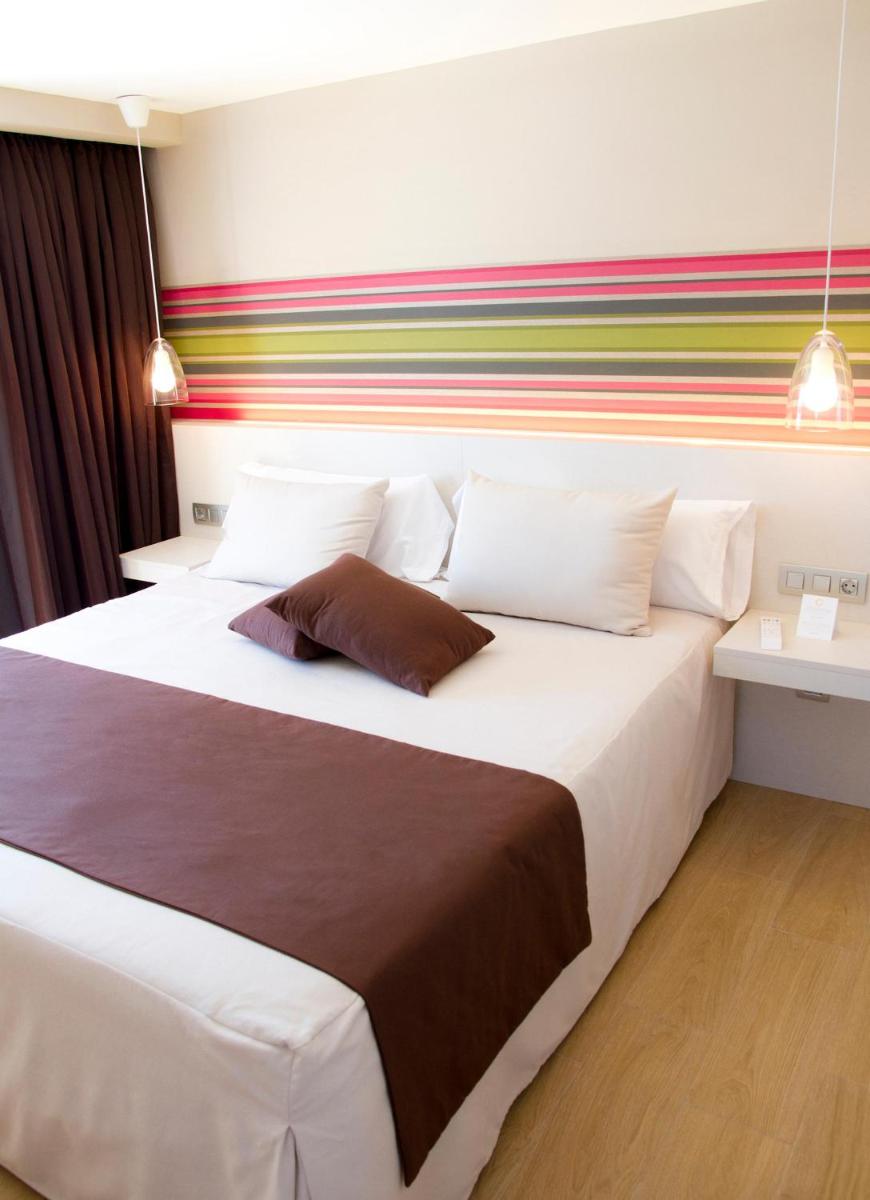 Un dormitorio con una gran cama blanca con una pared colorida. en ALEGRIA Plaza Paris 4*Sup, en Lloret de Mar