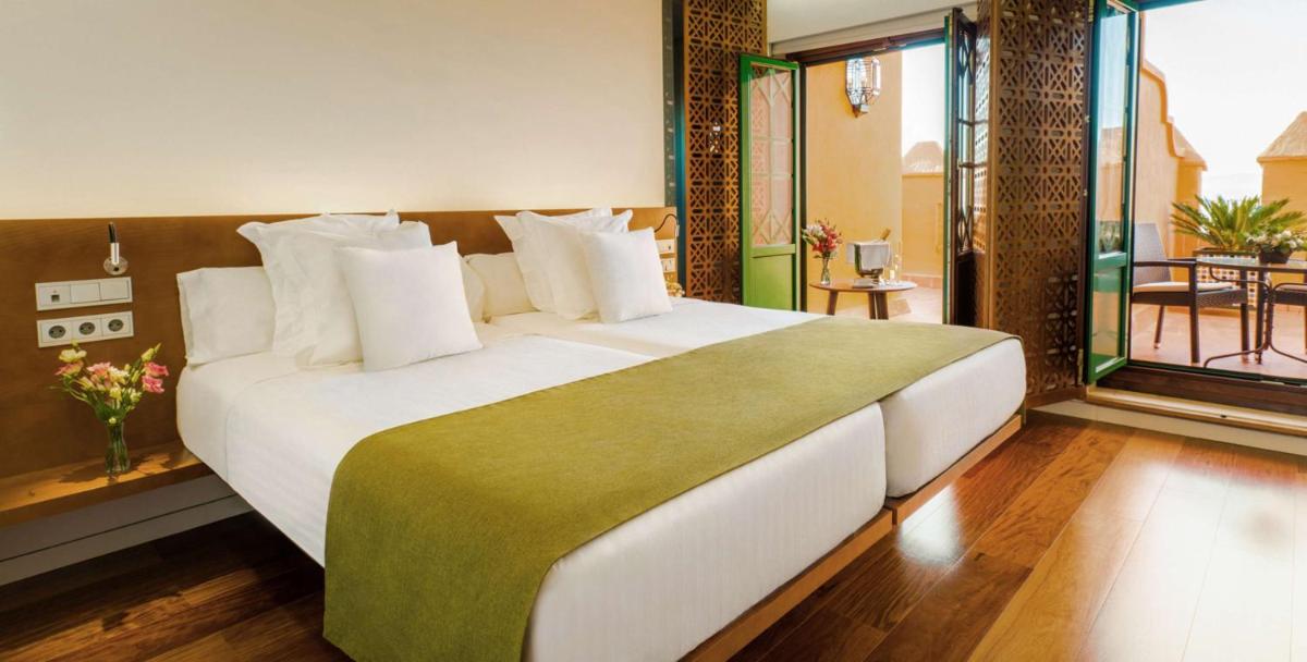 Cama blanca grande en habitación con balcón en Alhambra Palace Hotel, en Granada