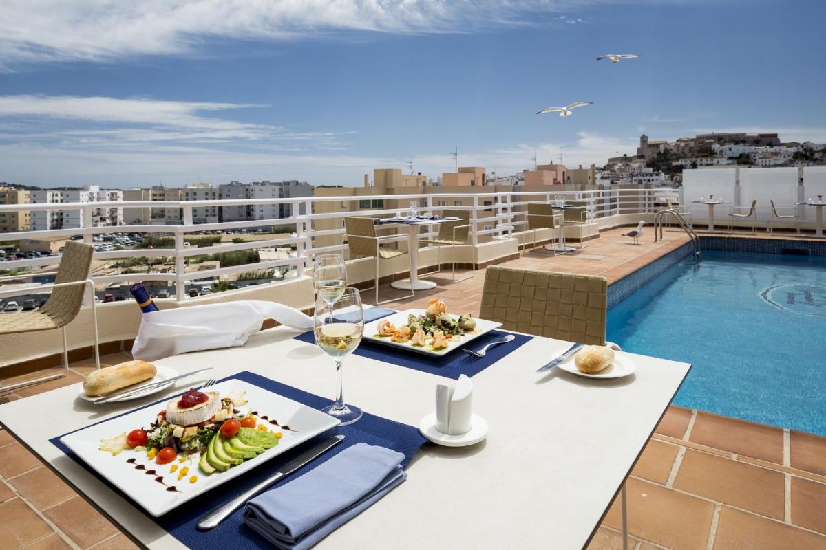 Una mesa con comida y vino en un balcón con piscina. en Hotel Royal Plaza, en Ibiza