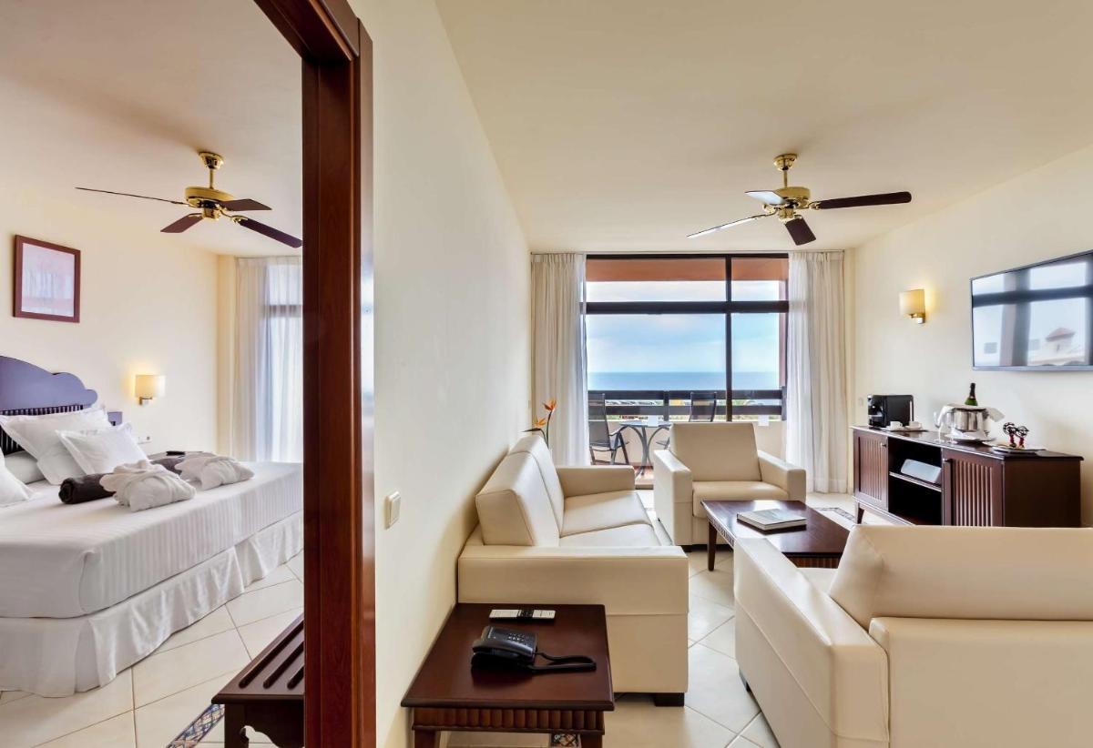 Una habitación de hotel con una cama y una sala de estar con un espejo. en Occidental Jandía Mar, en Morro del Jable