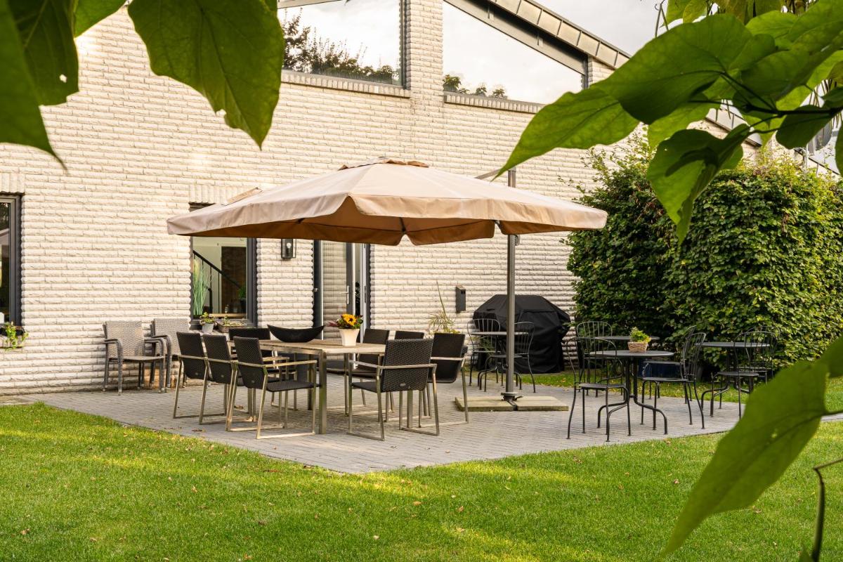 eine Terrasse mit Tischen und Stühlen und einem Sonnenschirm in der Unterkunft Motel Hasetal in Löningen