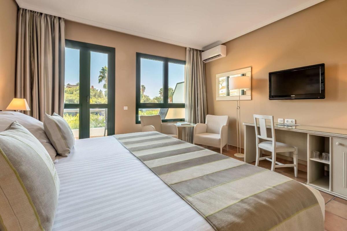 1 dormitorio con 1 cama grande, escritorio y TV en Barceló Jerez Montecastillo & Convention Center, en Jerez de la Frontera