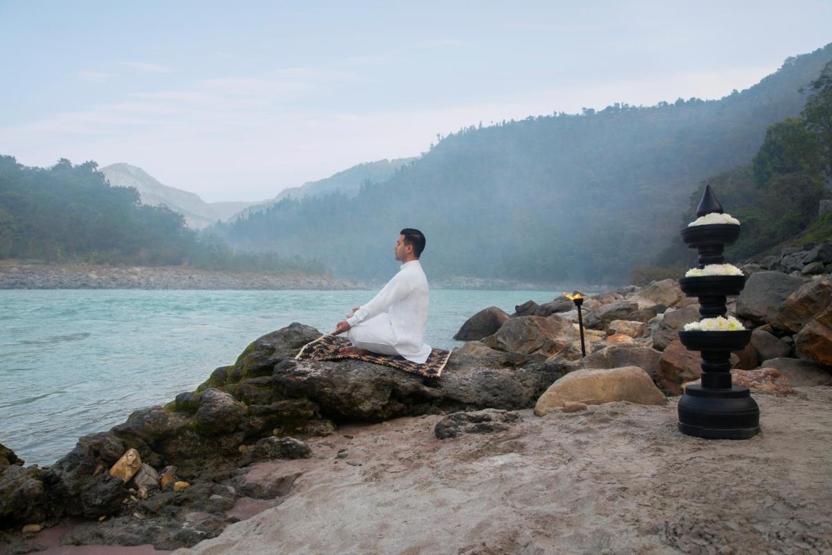 a man sitting on a rock next to a body of water at Anand Kashi by the Ganges Rishikesh - IHCL Seleqtions in Rishīkesh