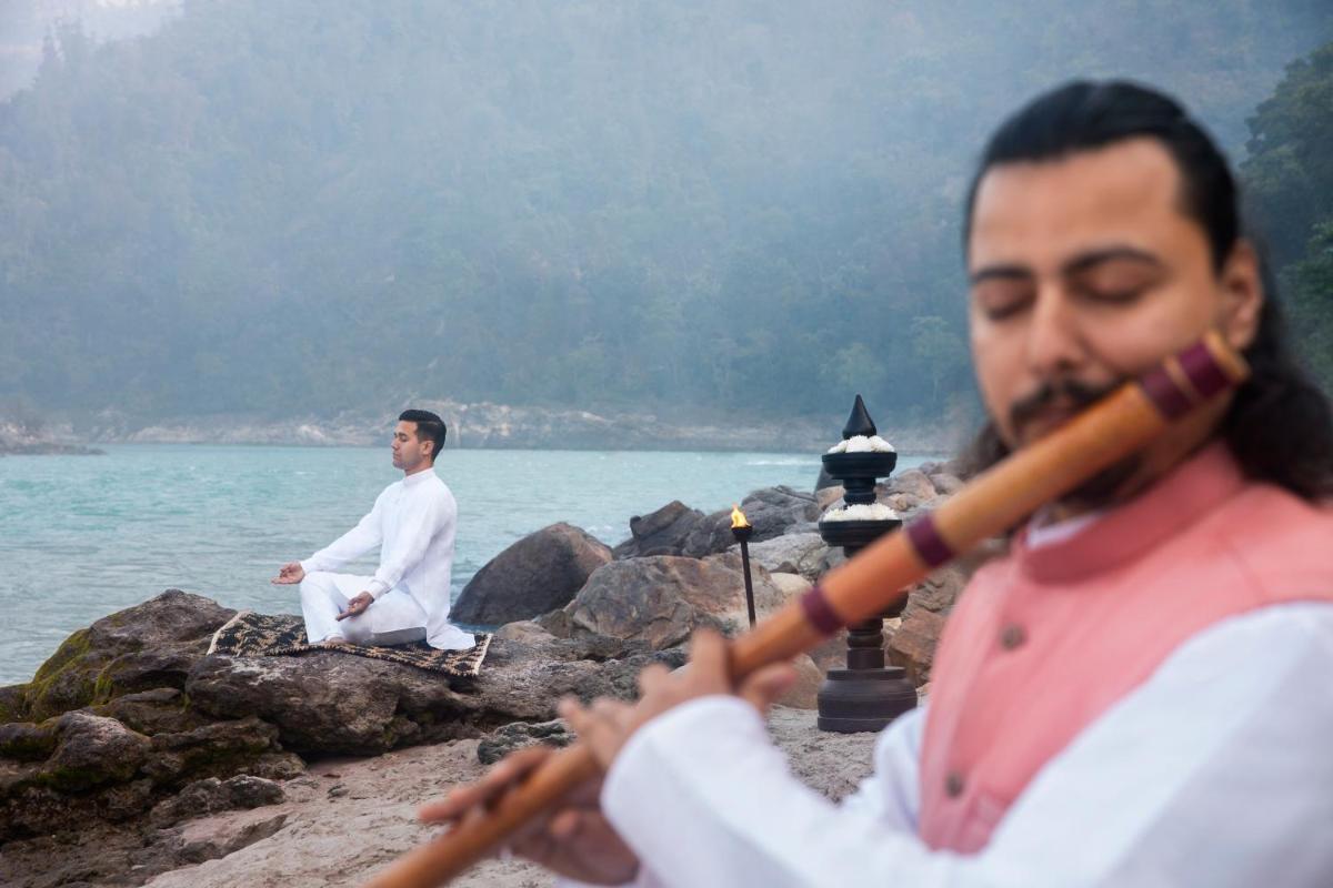two men are sitting on the rocks near the water at Anand Kashi by the Ganges Rishikesh - IHCL Seleqtions in Rishīkesh