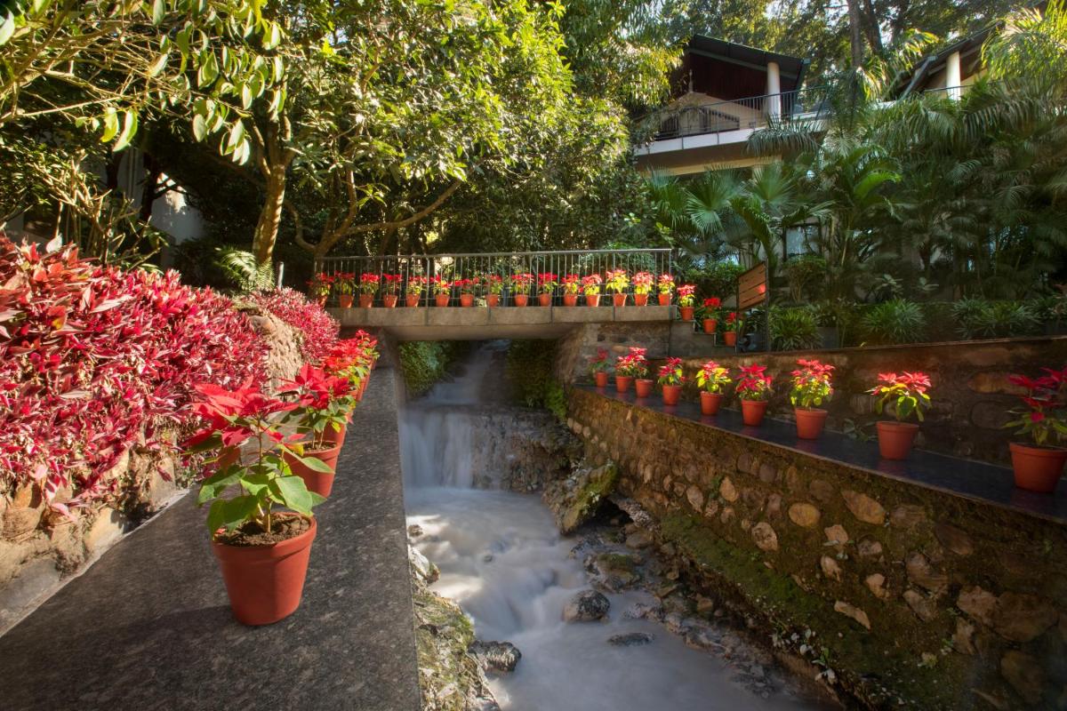 a bridge over a stream with flowers in pots at Anand Kashi by the Ganges Rishikesh - IHCL Seleqtions in Rishīkesh