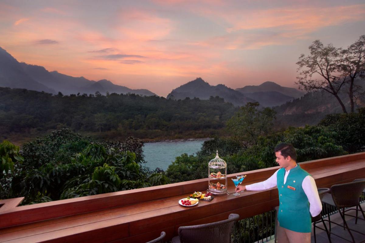 a woman standing on a balcony with a drink at Anand Kashi by the Ganges Rishikesh - IHCL Seleqtions in Rishīkesh