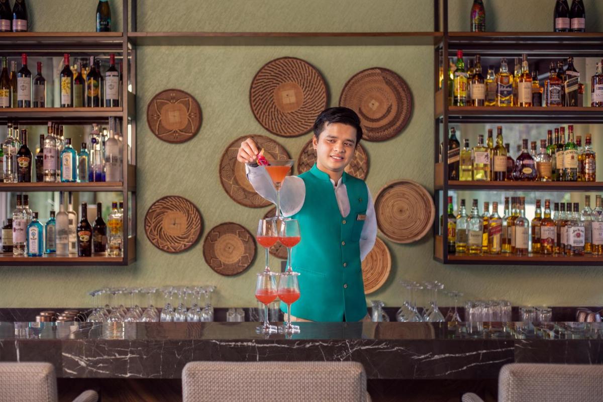 a woman standing behind a bar with a drink at Anand Kashi by the Ganges Rishikesh - IHCL Seleqtions in Rishīkesh