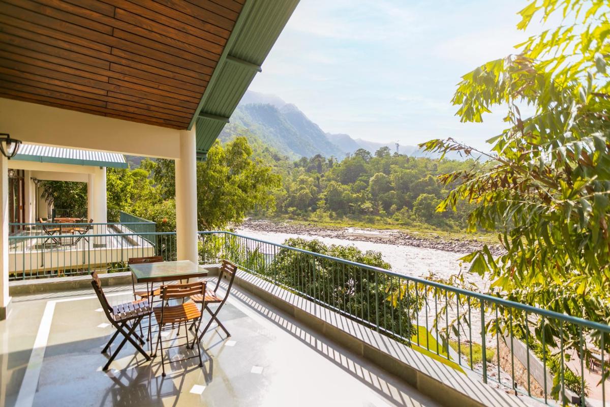 a balcony with a table and chairs overlooking a river at Anand Kashi by the Ganges Rishikesh - IHCL Seleqtions in Rishīkesh