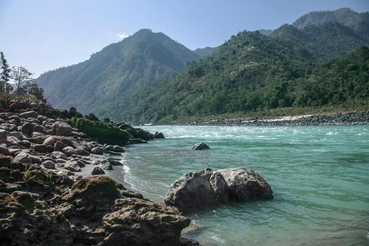a river with rocks and mountains in the background at Anand Kashi by the Ganges Rishikesh - IHCL Seleqtions in Rishīkesh