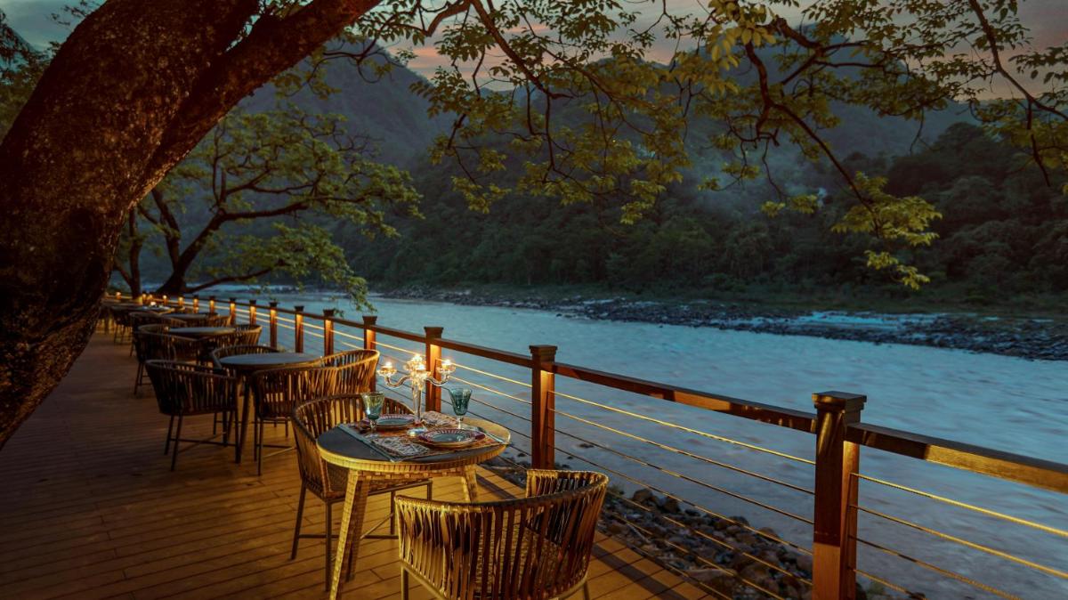 a row of tables and chairs on a deck next to a river at Anand Kashi by the Ganges Rishikesh - IHCL Seleqtions in Rishīkesh