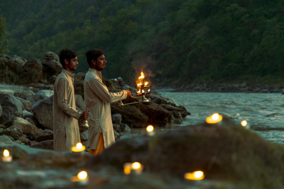 two men holding candles on a beach with water at Anand Kashi by the Ganges Rishikesh - IHCL Seleqtions in Rishīkesh