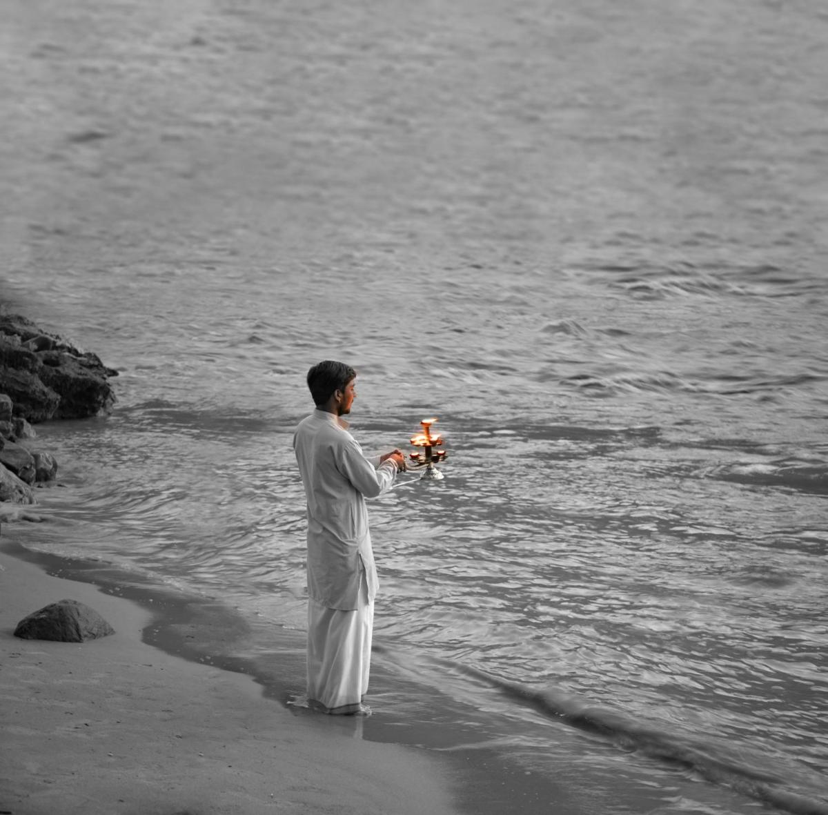 a man standing on the beach holding a candle at Anand Kashi by the Ganges Rishikesh - IHCL Seleqtions in Rishīkesh