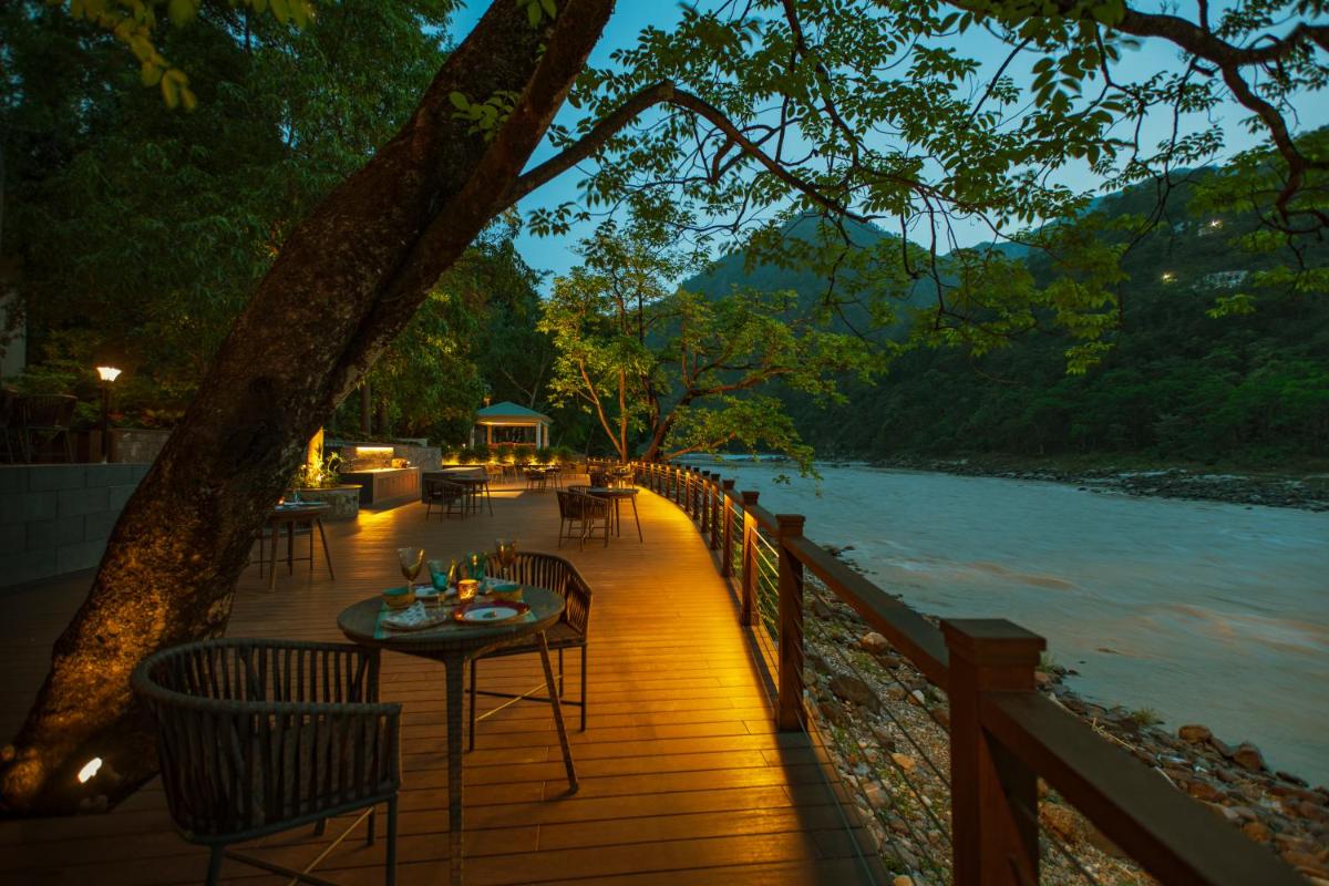 a wooden deck with a table and chairs next to a river at Anand Kashi by the Ganges Rishikesh - IHCL Seleqtions in Rishīkesh