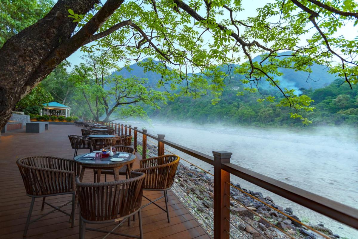 a patio with tables and chairs next to a river at Anand Kashi by the Ganges Rishikesh - IHCL Seleqtions in Rishīkesh