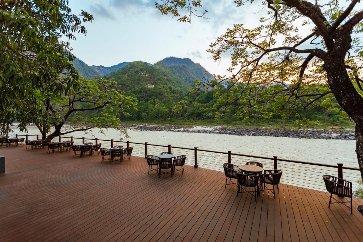 a wooden deck with tables and chairs next to a river at Anand Kashi by the Ganges Rishikesh - IHCL Seleqtions in Rishīkesh
