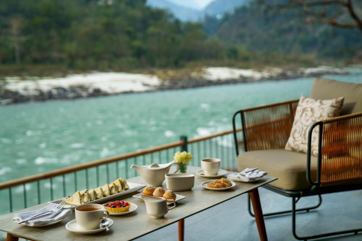 a table with food on a balcony with a view of a river at Anand Kashi by the Ganges Rishikesh - IHCL Seleqtions in Rishīkesh