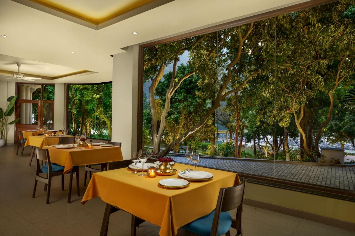 a restaurant with tables and chairs and large windows at Anand Kashi by the Ganges Rishikesh - IHCL Seleqtions in Rishīkesh