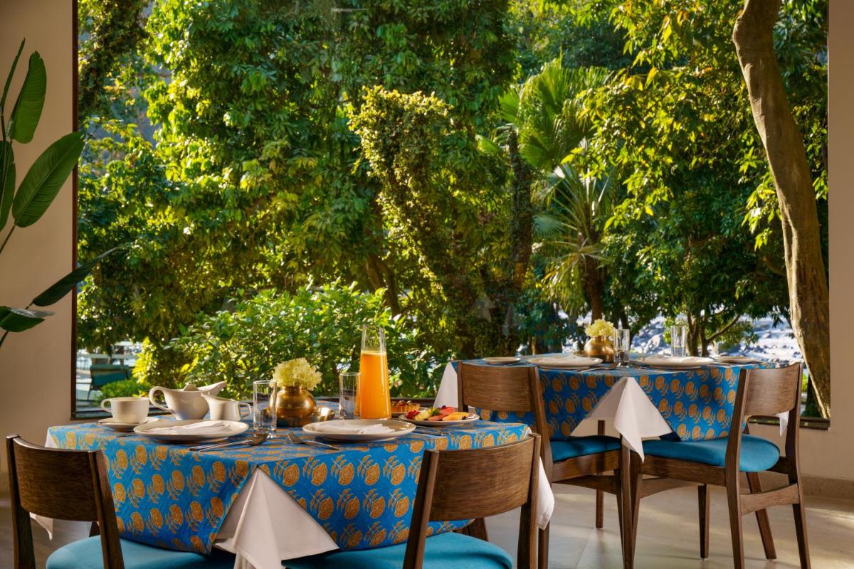 a table with a blue tablecloth and chairs with trees at Anand Kashi by the Ganges Rishikesh - IHCL Seleqtions in Rishīkesh