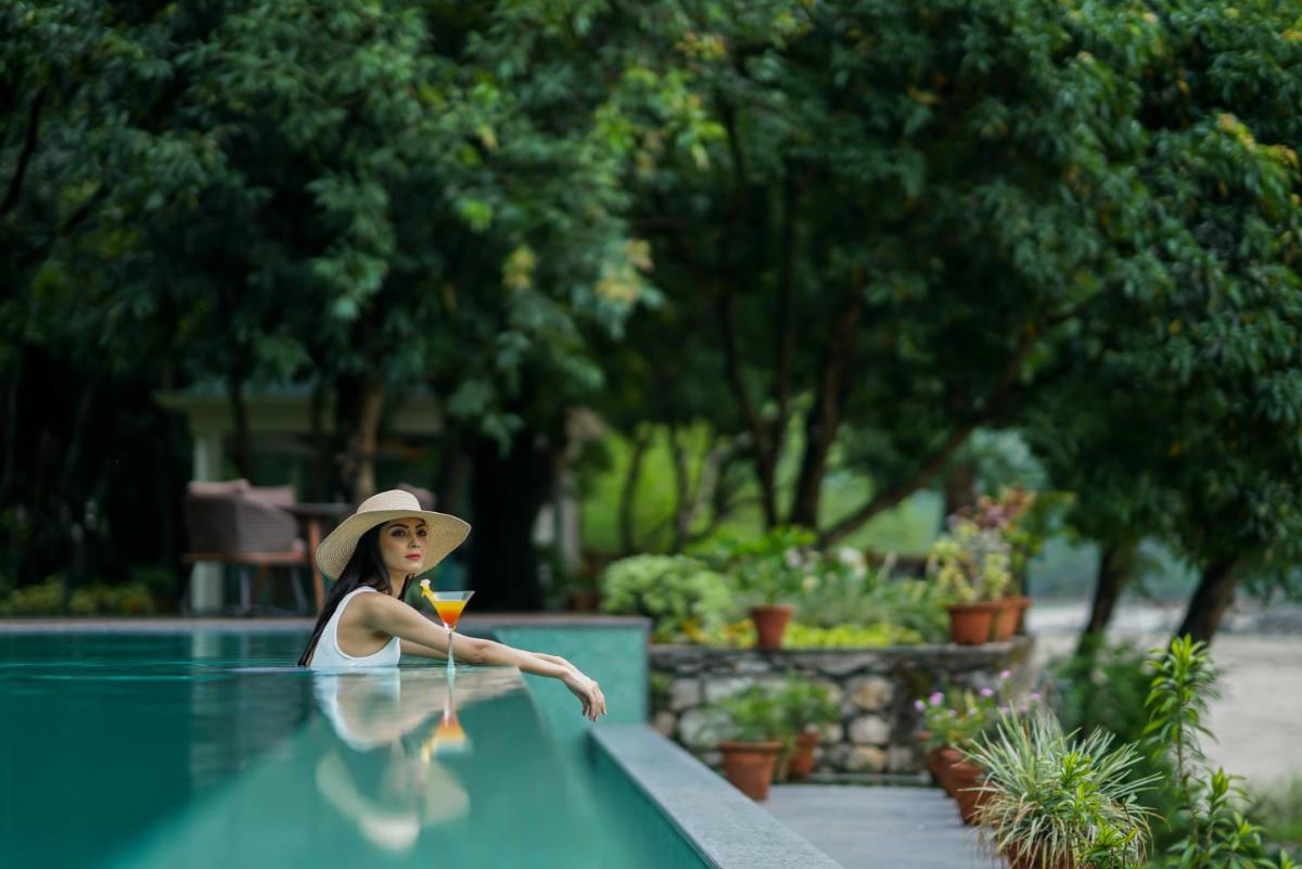 a woman in a hat sitting next to a swimming pool at Anand Kashi by the Ganges Rishikesh - IHCL Seleqtions in Rishīkesh
