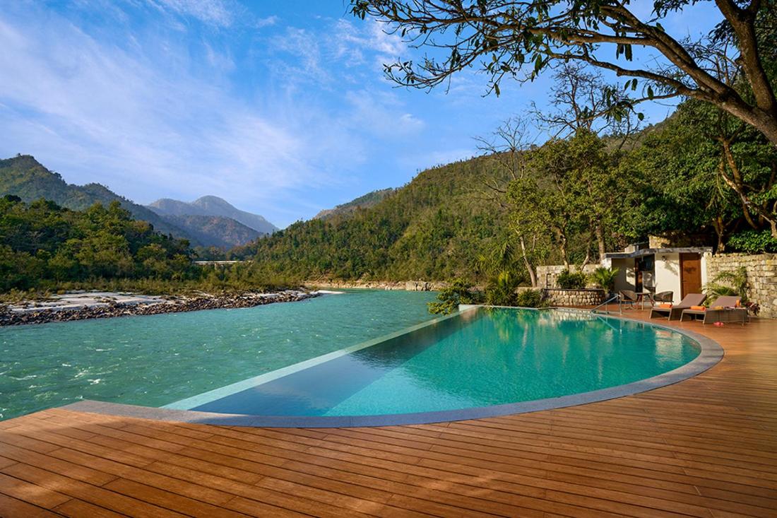 a swimming pool on a wooden deck next to a river at Anand Kashi by the Ganges Rishikesh - IHCL Seleqtions in Rishīkesh