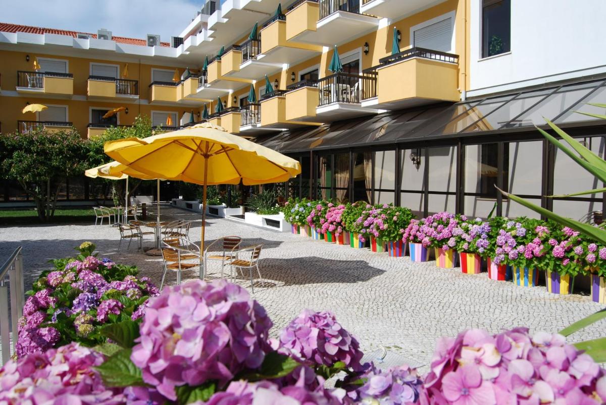 um guarda-chuva e algumas flores em frente a um edifício em D. Afonso Hotel & SPA em Monte Real