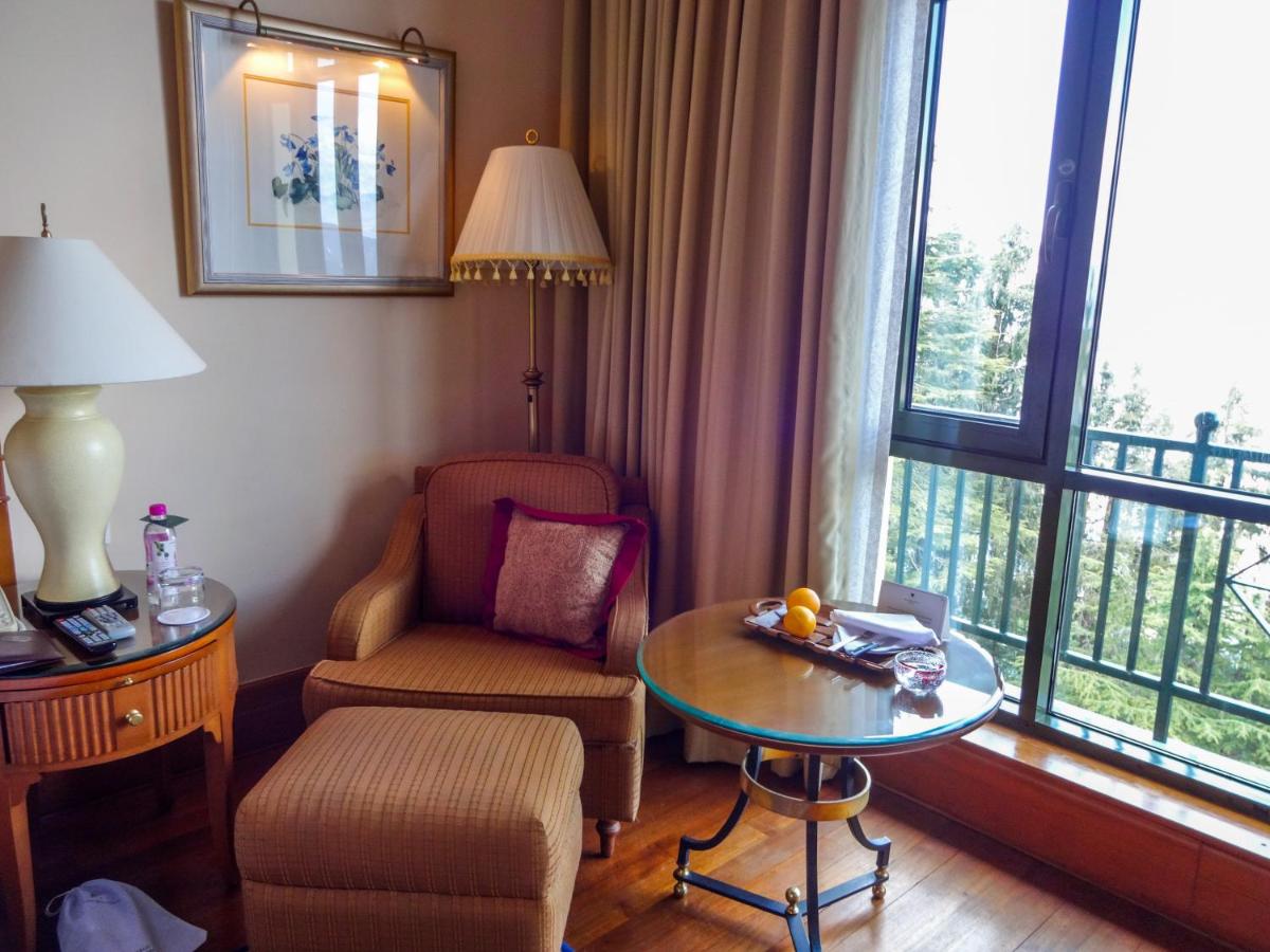 a living room with a table and a chair and a window at Wildflower Hall, An Oberoi Resort, Shimla in Shimla