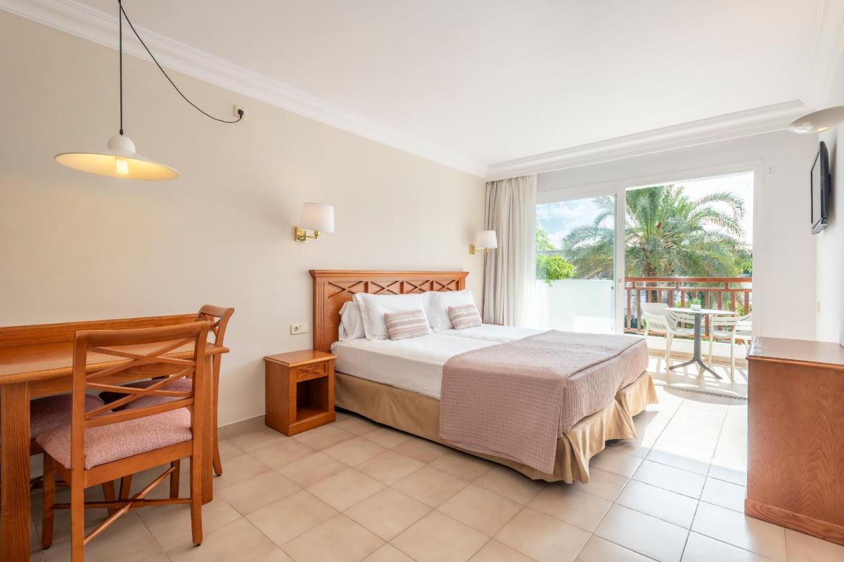 Un dormitorio con una cama y un escritorio y un balcón. en Inturotel Cala Azul, en Cala d´Or