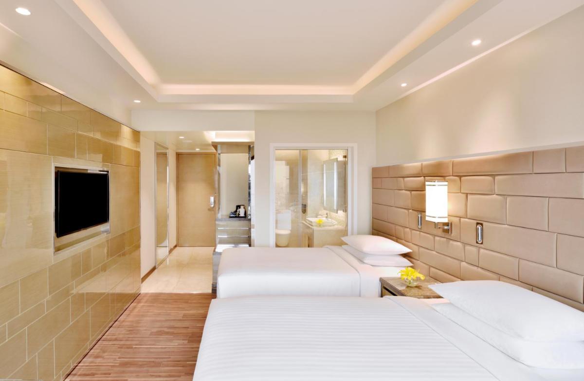 a hotel room with three beds and a television at Courtyard by Marriott Bengaluru Hebbal in Bengaluru