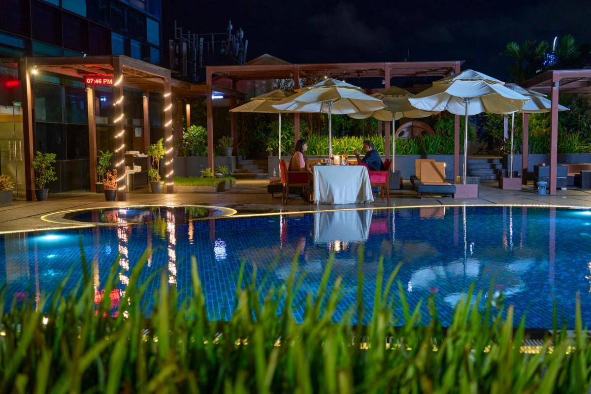 a pool at night with people sitting at a table and umbrellas at The Raviz Calicut in Kozhikode
