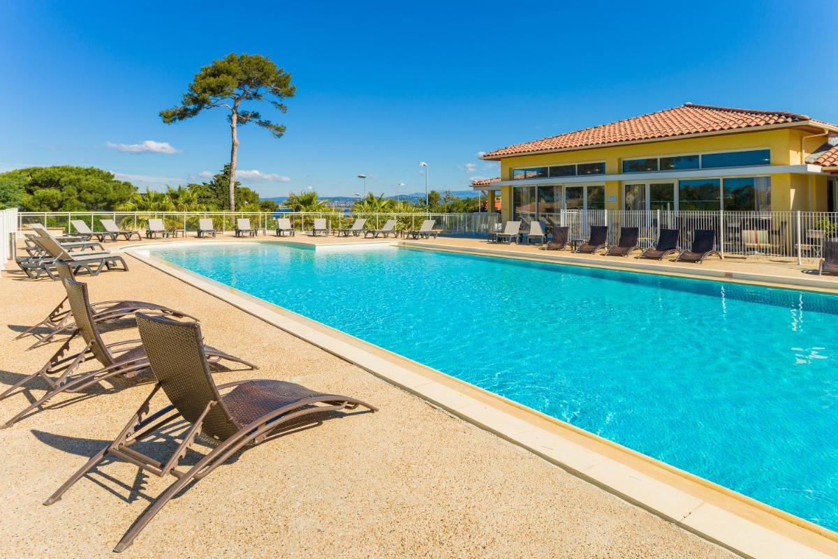 une piscine avec des chaises et un bâtiment dans l'établissement Lagrange Vacances Les Terrasses des Embiez, à Six-Fours-les-Plages