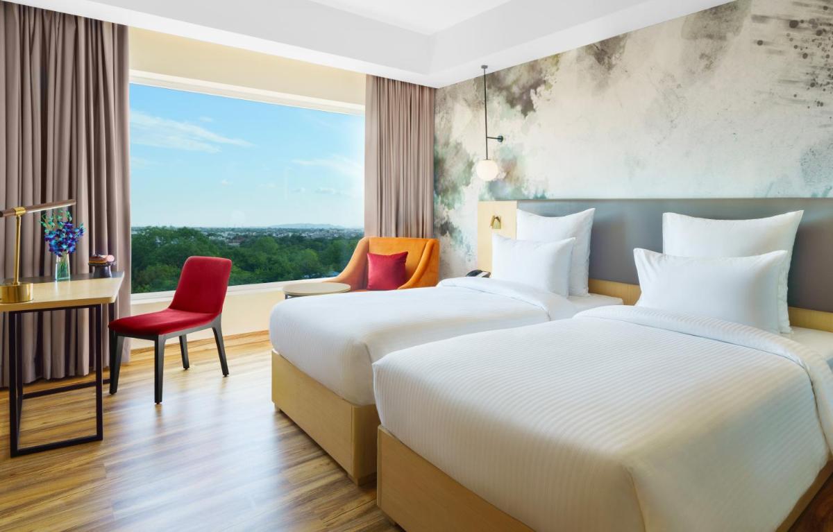 two beds in a hotel room with a window at Novotel Jaipur Convention Centre in Jaipur