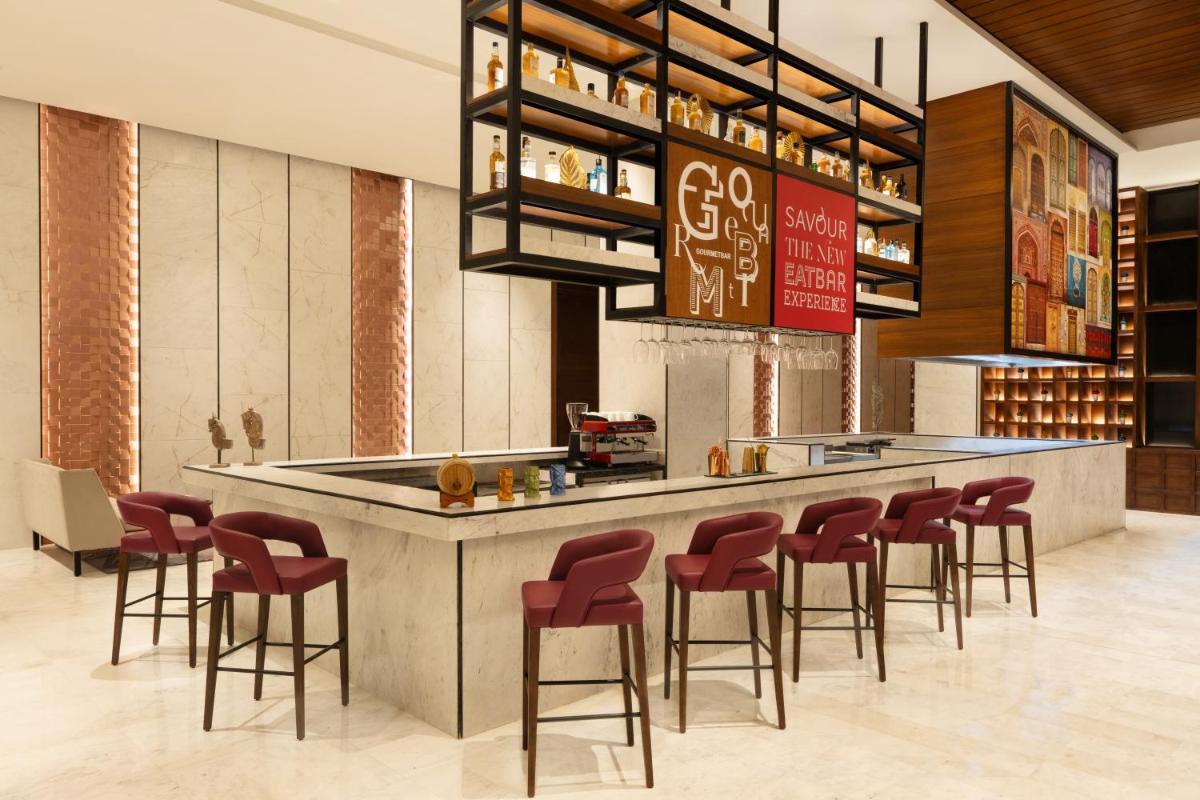 a restaurant with a bar with red stools at Novotel Jaipur Convention Centre in Jaipur