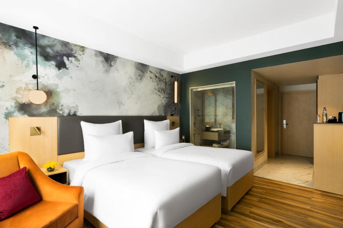 a bedroom with a large white bed and a chair at Novotel Jaipur Convention Centre in Jaipur