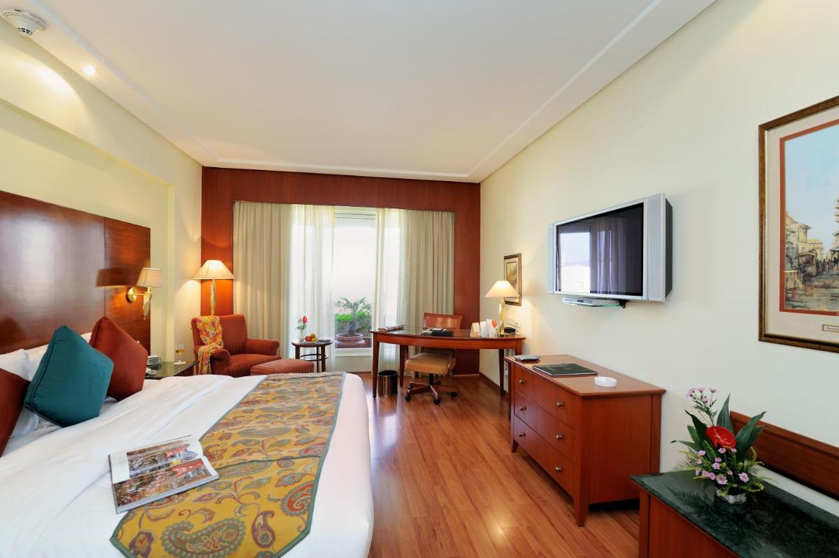 a hotel room with a bed and a desk and a television at The Lalit Mumbai in Mumbai
