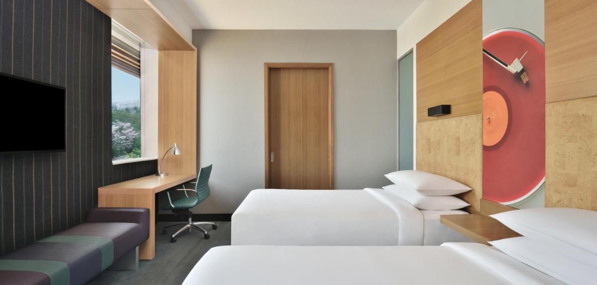 a hotel room with two beds and a desk and a tv at Aloft Bengaluru Outer Ring Road in Bengaluru