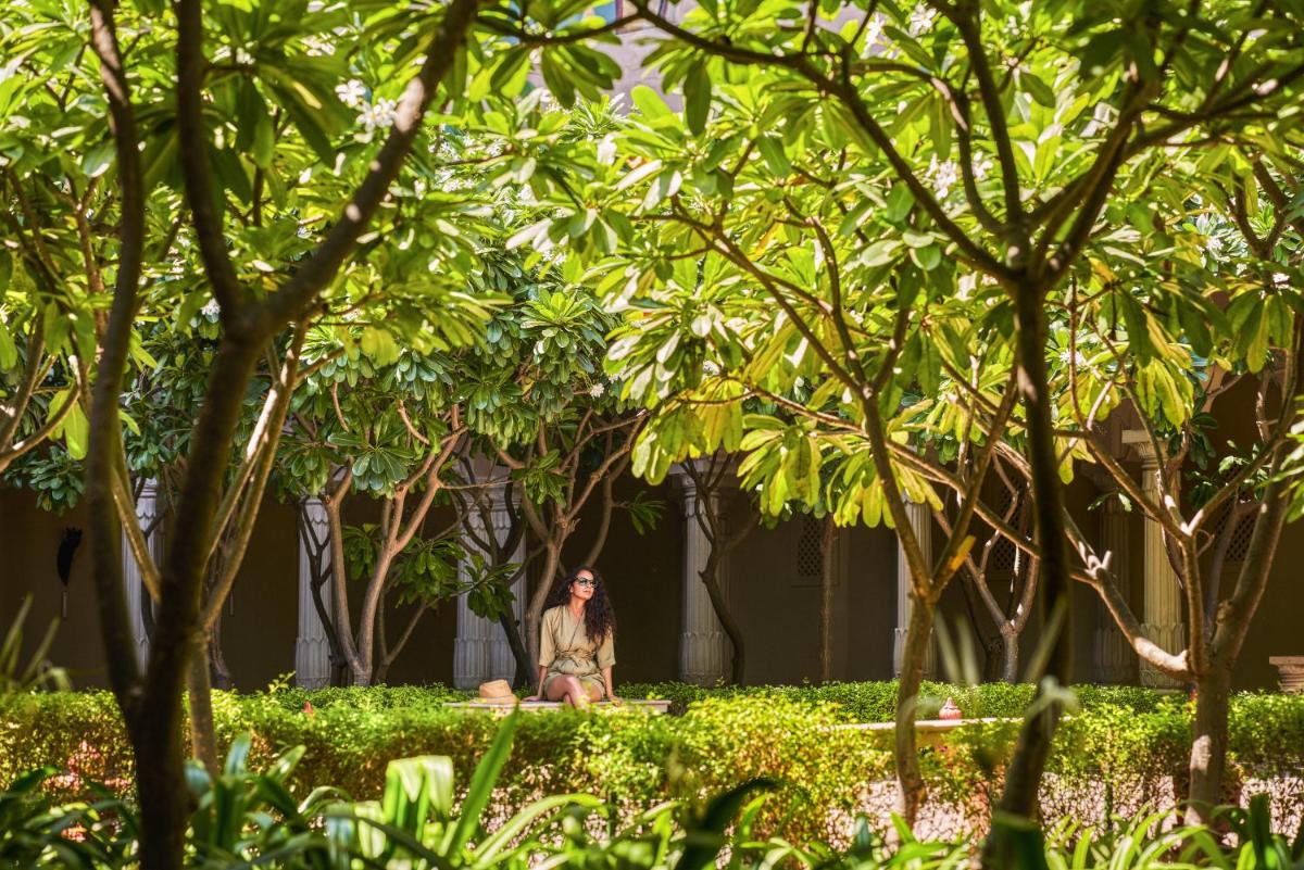 a woman sitting on a bench in a park with trees at Fairmont Jaipur in Jaipur