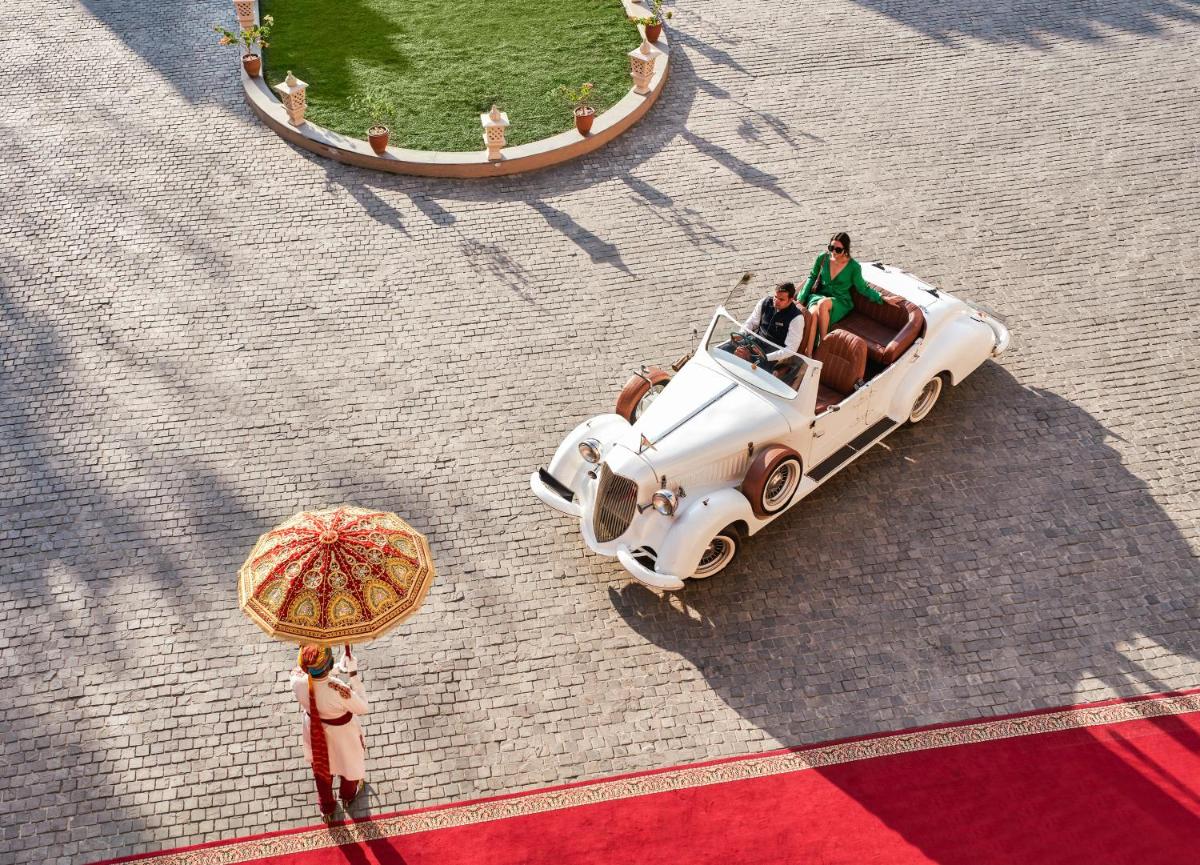 an old white car driving down a street with a man at Fairmont Jaipur in Jaipur