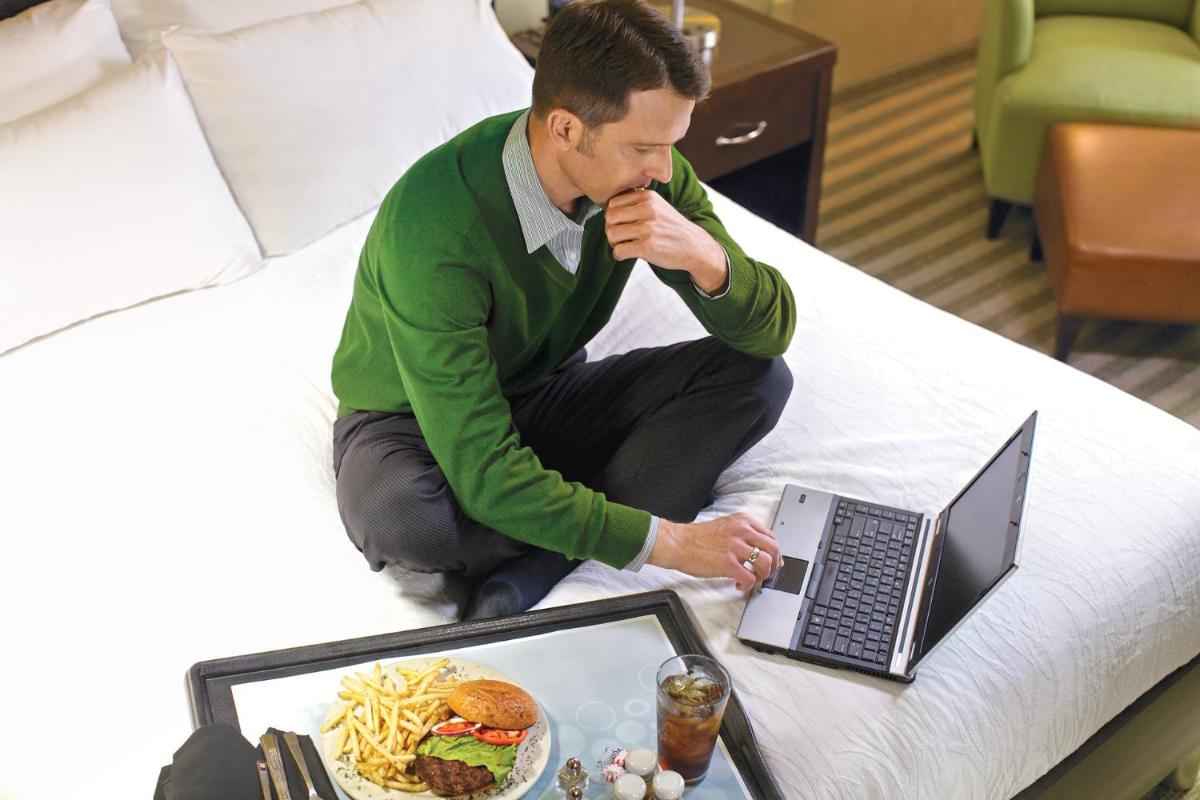 a man sitting on a bed with a laptop and a plate of food at Hilton Garden Inn, Trivandrum in Trivandrum