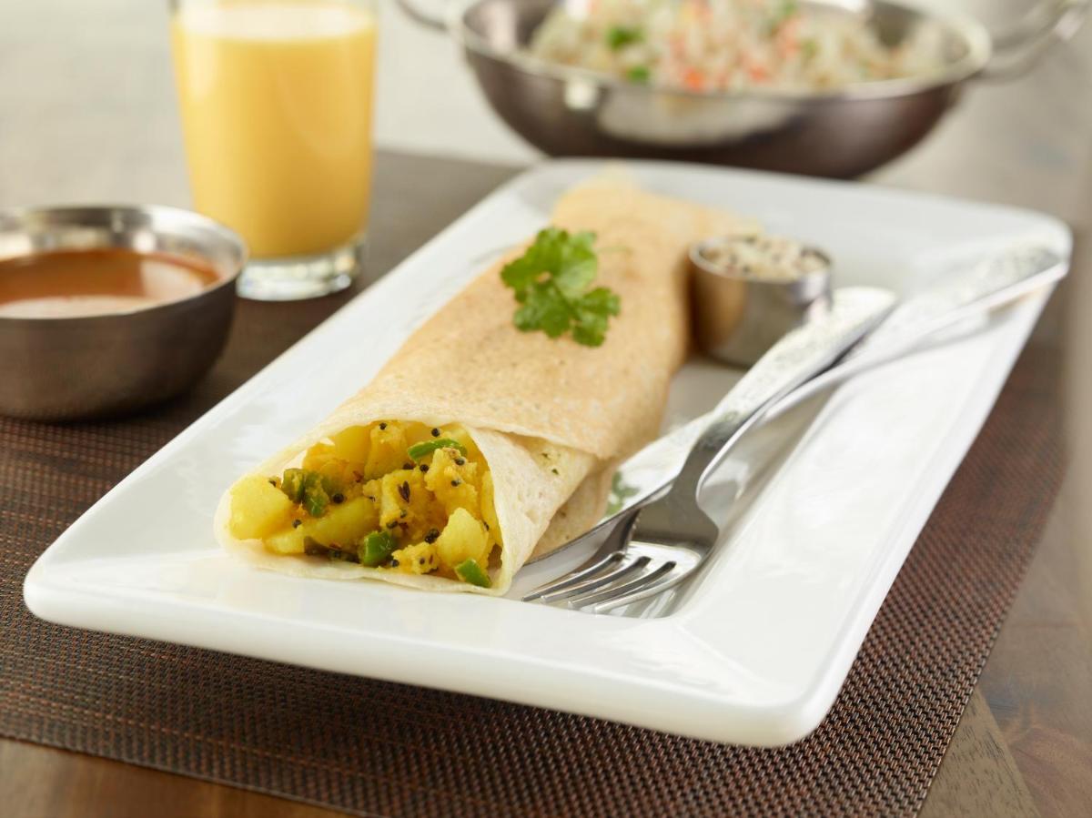 a white plate with a burrito and a fork at Hilton Garden Inn, Trivandrum in Trivandrum