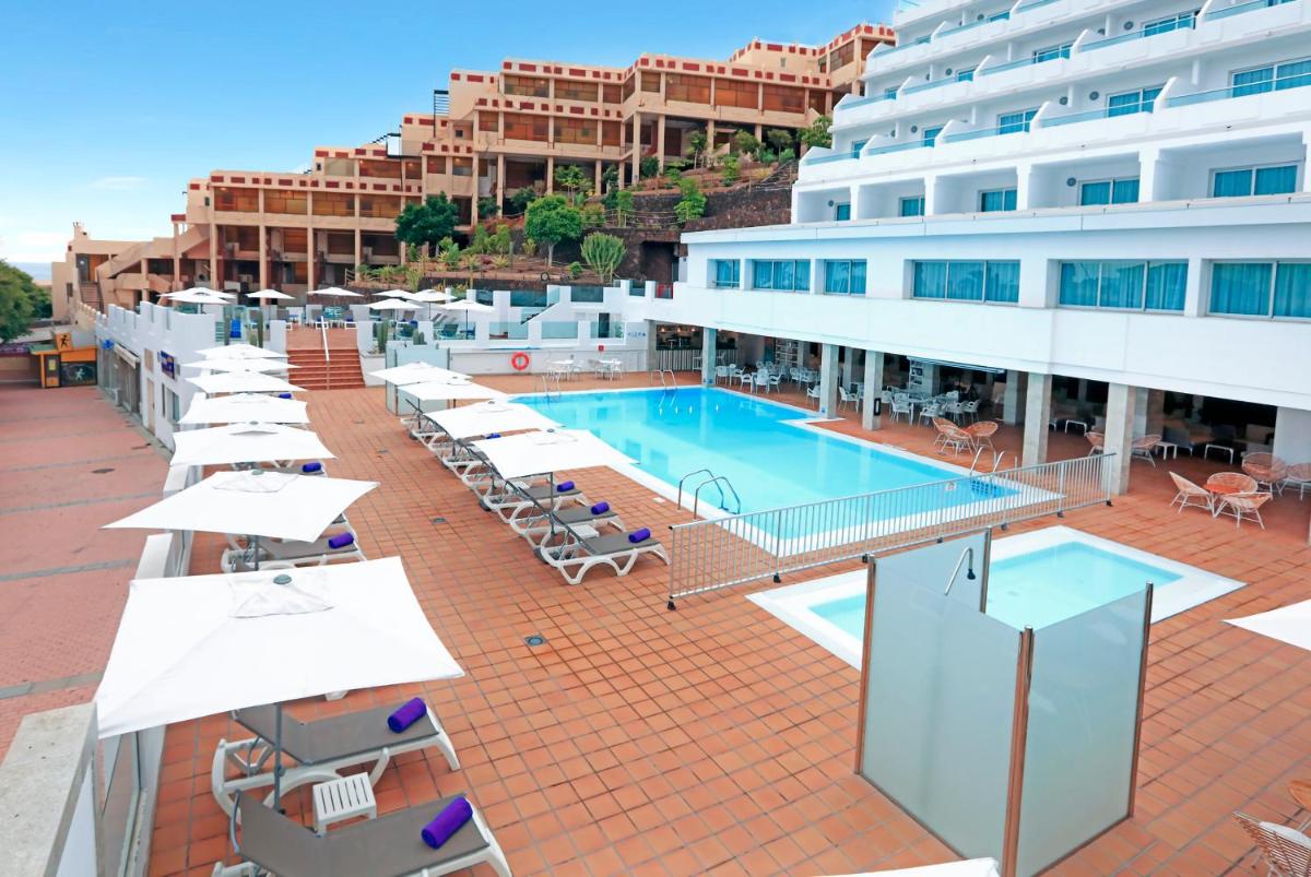 Una piscina de hotel con tumbonas y sombrillas. en FERGUS Cactus Garden, en Playa de Jandía