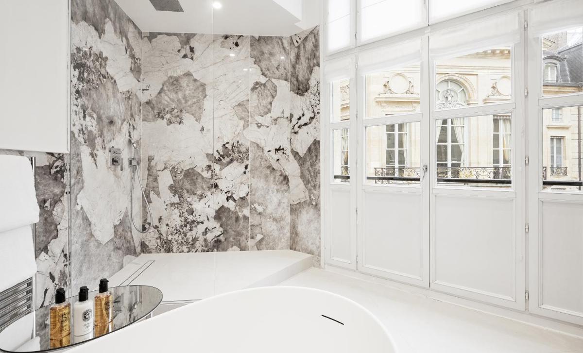 La salle de bains est pourvue d'une baignoire blanche et d'un mur en marbre. dans l'établissement Grand Hôtel Du Palais Royal, à Paris