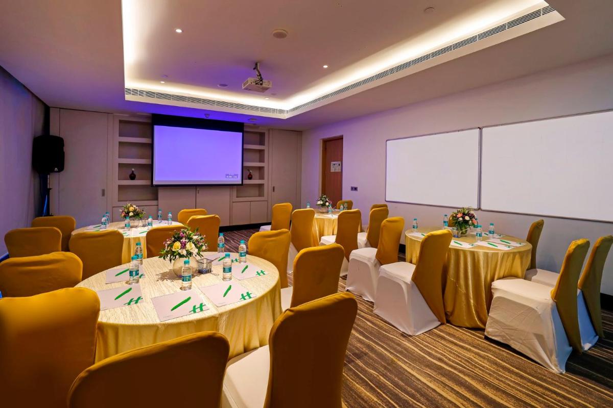 a conference room with tables and chairs and a screen at Holiday Inn Chennai OMR IT Expressway by IHG in Chennai