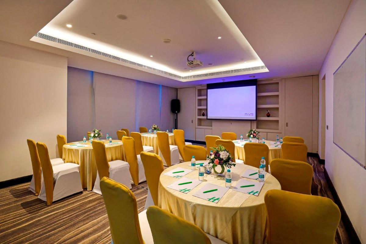 a conference room with tables and chairs and a screen at Holiday Inn Chennai OMR IT Expressway by IHG in Chennai