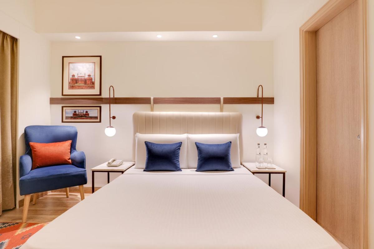 a bedroom with a large bed and two blue chairs at Lemon Tree Premier, Delhi Airport in New Delhi a bedroom with a large bed and two blue chairs at Lemon Tree Premier, Delhi Airport in New Delhi