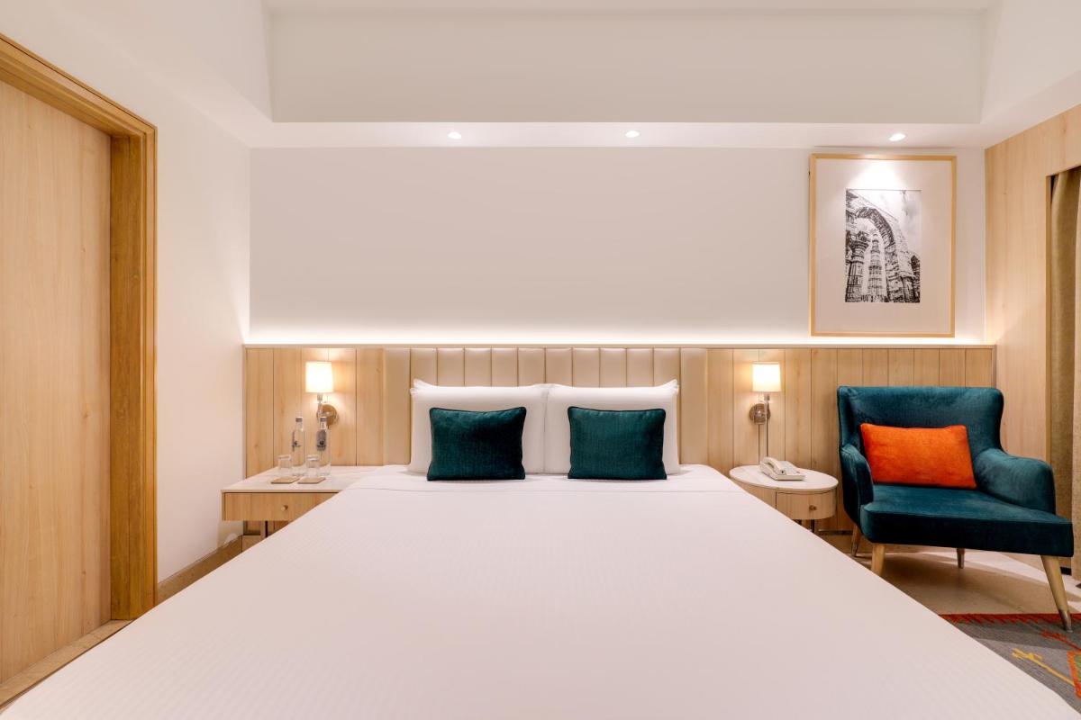 a bedroom with a large bed with two blue chairs at Lemon Tree Premier, Delhi Airport in New Delhi a bedroom with a large bed with two blue chairs at Lemon Tree Premier, Delhi Airport in New Delhi