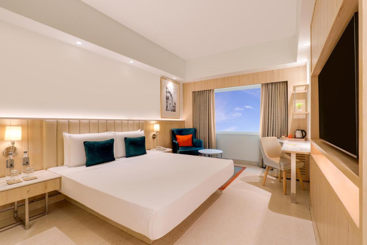 a hotel room with a large bed and a desk at Lemon Tree Premier, Delhi Airport in New Delhi a hotel room with a large bed and a desk at Lemon Tree Premier, Delhi Airport in New Delhi