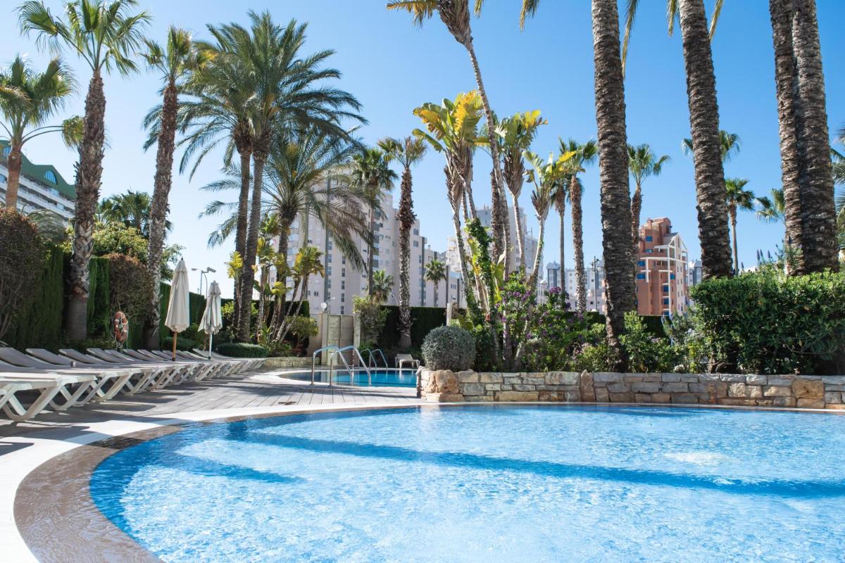 una piscina con palmeras al fondo en AR Diamante Beach & SPA Hotel 4 SUP, en Calpe