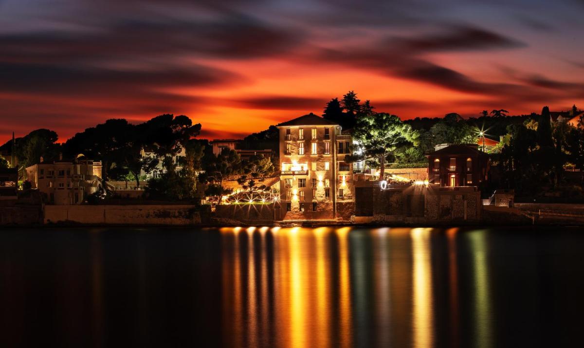 un bâtiment avec des lumières sur l'eau la nuit dans l'établissement Splendid Hôtel & Spa, à Bandol