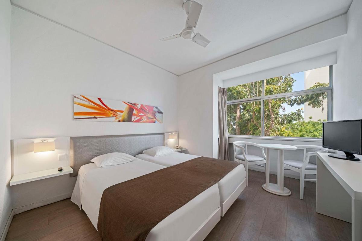 um quarto com uma cama, uma mesa e uma janela em Dorisol Estrelicia Hotel no Funchal
