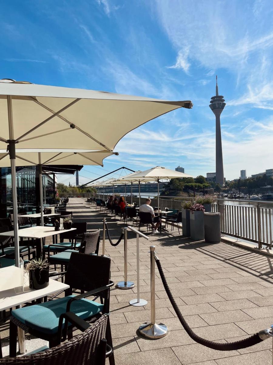 eine Terrasse mit Tischen und Sonnenschirmen und einem Turm im Hintergrund in der Unterkunft Hyatt Regency Dusseldorf in Düsseldorf